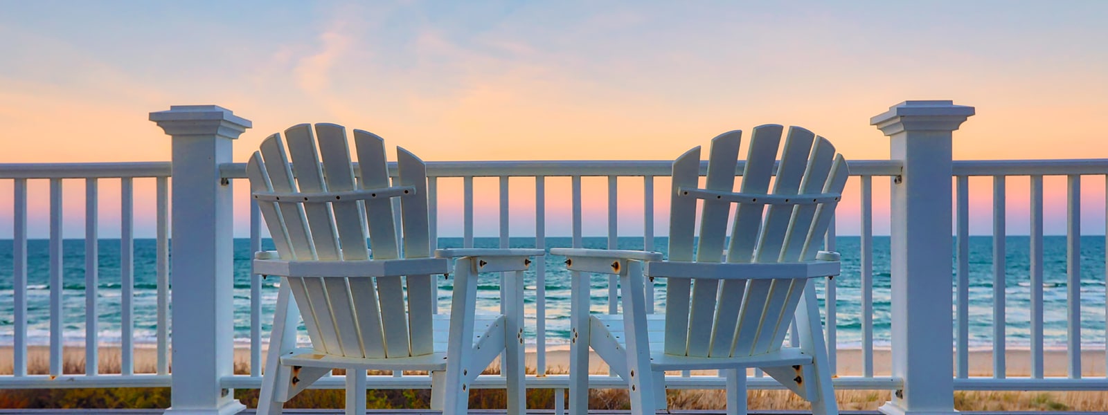 Two empty Adirondack chair on a balcony deck overlooking the beach and the ocean in the Outer Banks of North Carolina