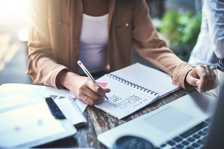 Woman sitting in front of laptop and writing in notebook