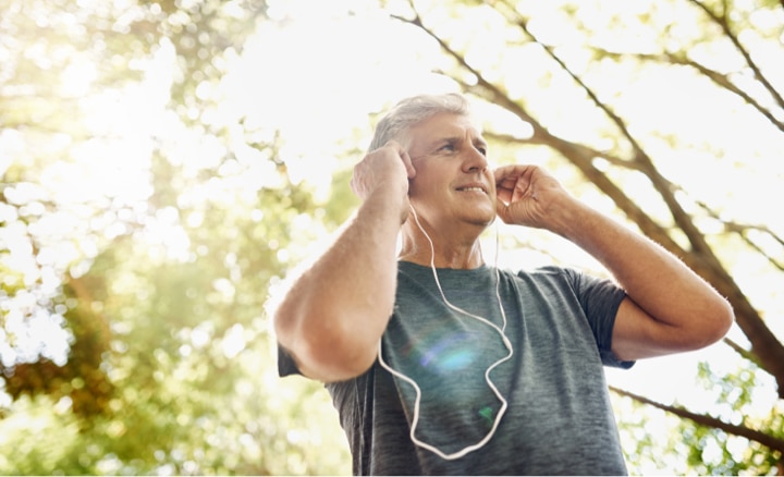 Older man standing in the sunlight and putting in earbuds