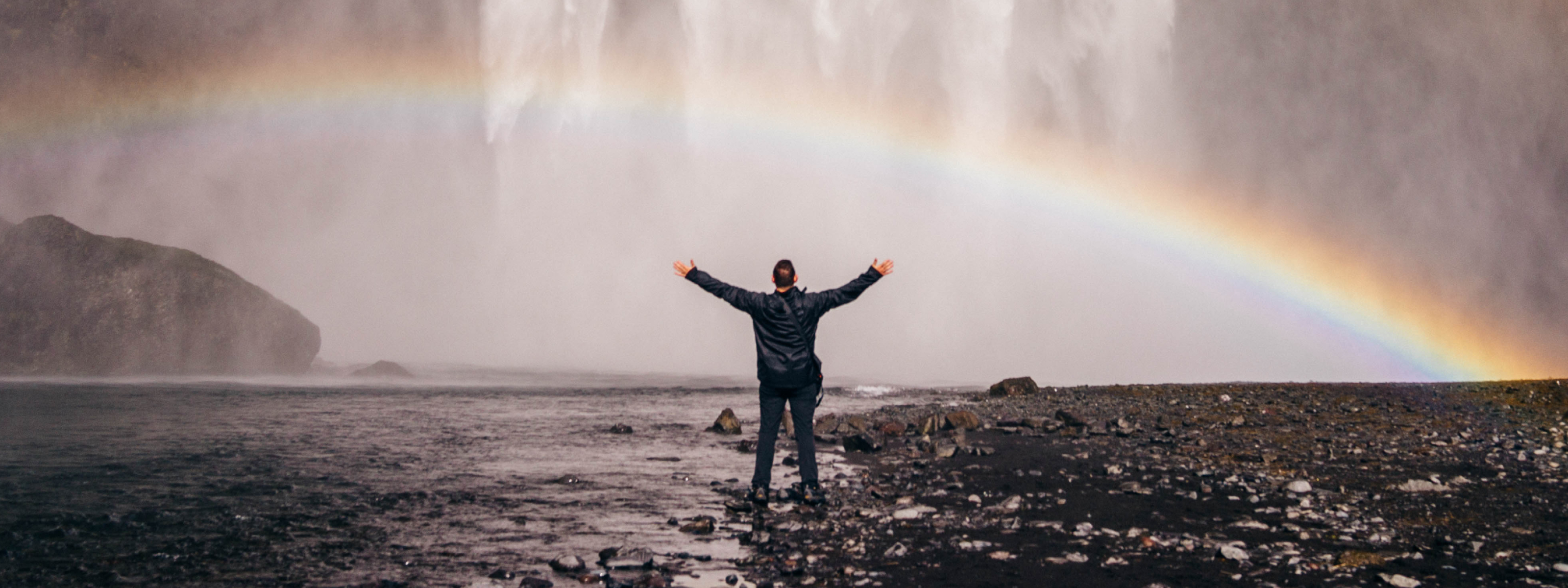man standing in front of a waterfall and rainbow