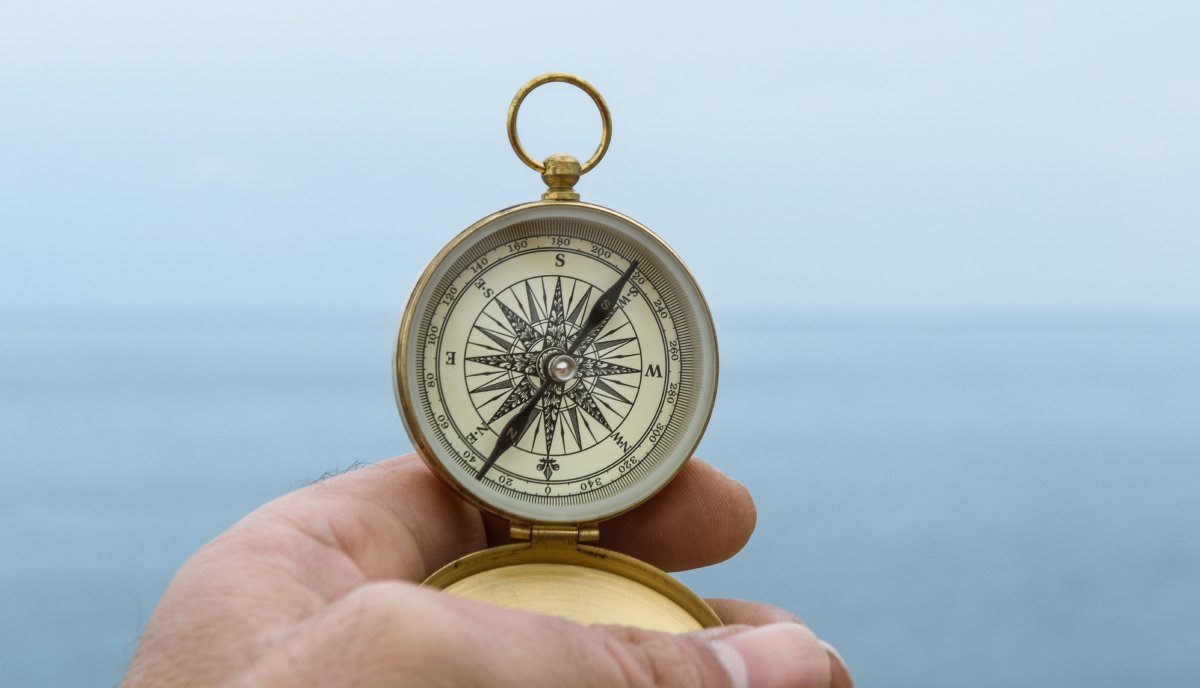a hand holding a compass with the sea in the background